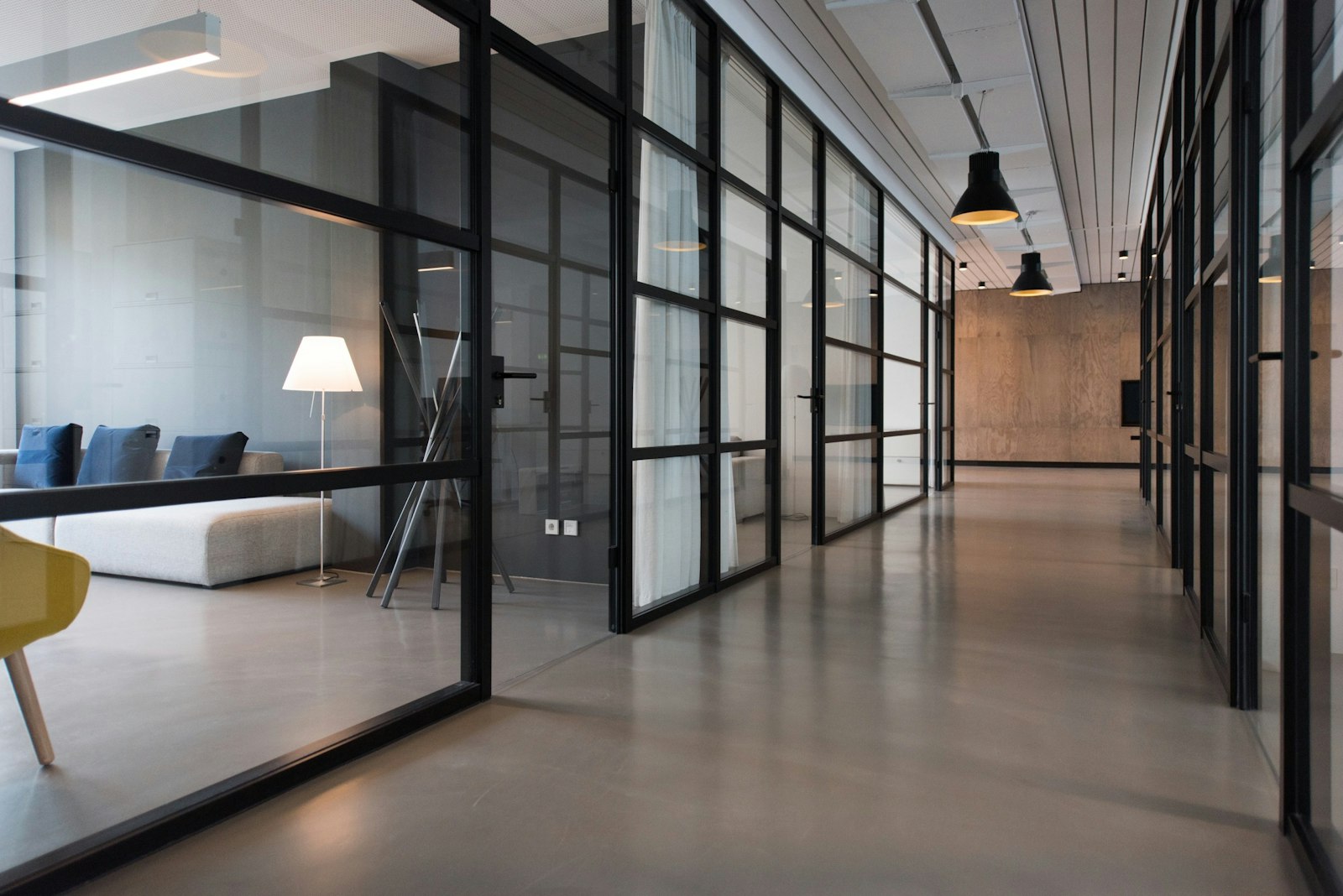 A modern open office interior with glass partitions and warm concrete walls.